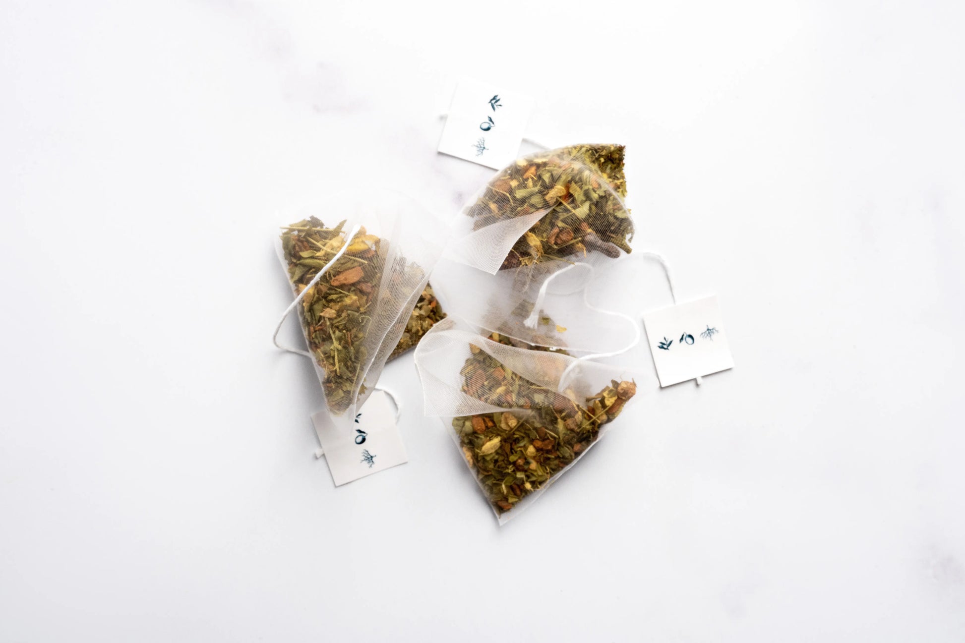 Three pyramid tea sachet bags filled with organic herbal blend on a white background.