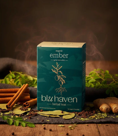Organic Ember herbal tea sachet box featuring cinnamon sticks, ginger, and botanicals on a rustic wooden surface with rising steam.